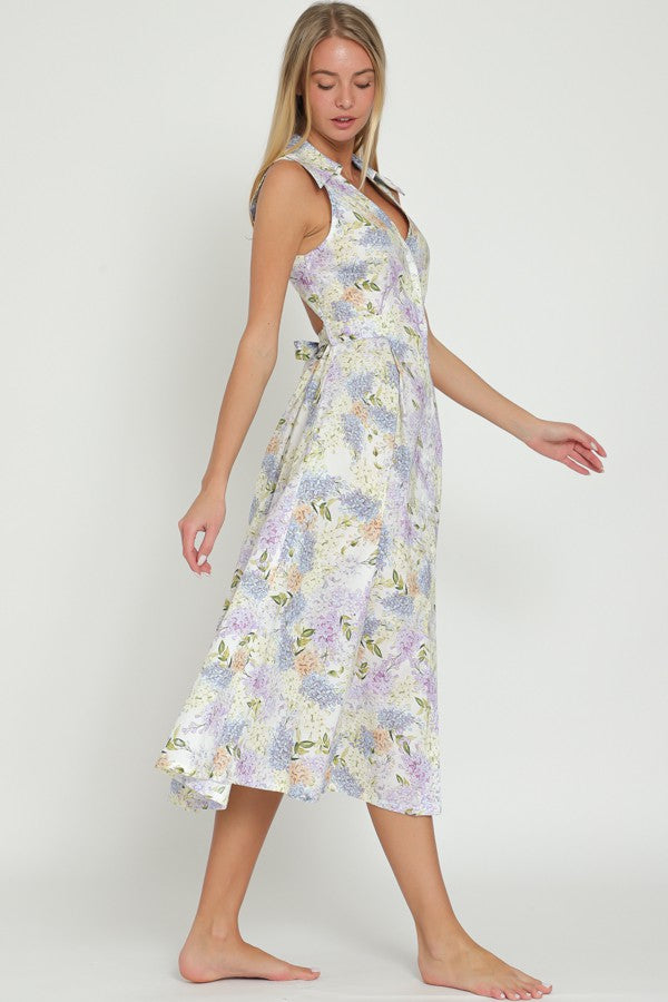 woman wearing a lavender floral midi dress with a wrap design and tie detail at the waist, standing barefoot