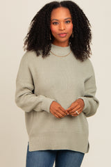 woman wearing a light green oversized knit sweater with a high neckline and side slits, paired with jeans
