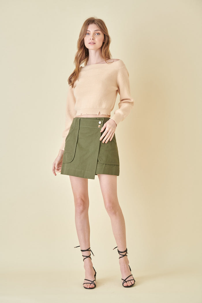 woman wearing a beige cropped sweater and an olive green mini skirt with front pockets and button details
