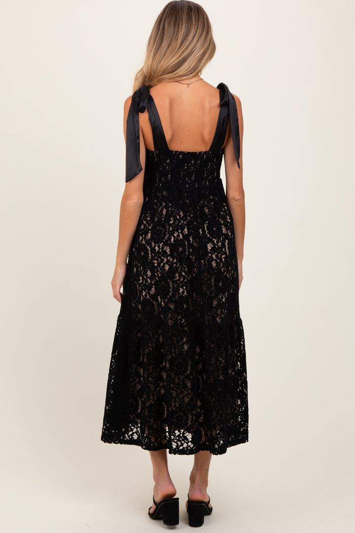 woman wearing a black lace maternity dress with satin ribbon straps, showing a flowing skirt and open back design