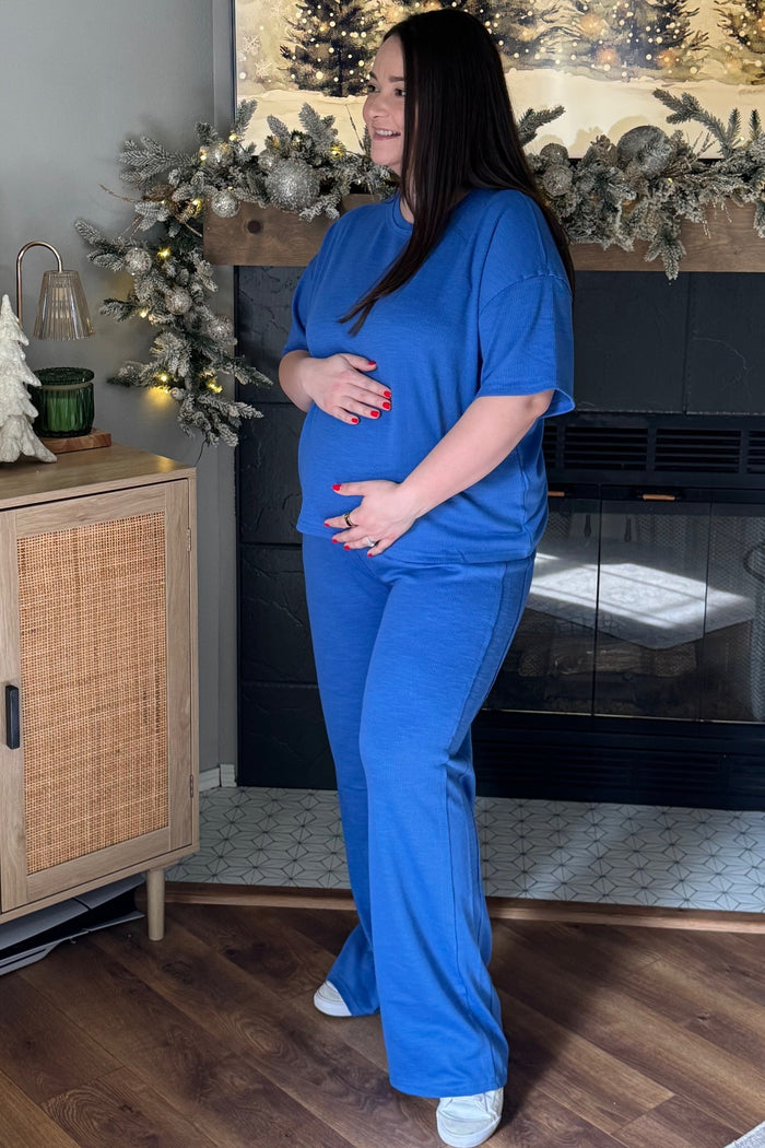 woman wearing a blue maternity loungewear set, cradling her baby bump while standing by a fireplace