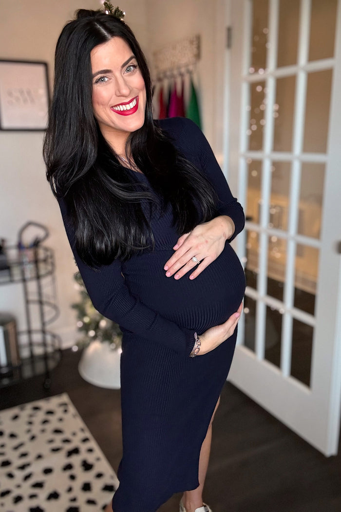 woman wearing a navy blue maternity dress with a side slit, standing and cradling her baby bump