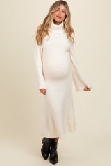 woman wearing a cream turtleneck maternity sweater dress with bell sleeves and a visible baby bump