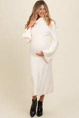 woman wearing a cream long sleeve maternity dress with a cowl neck, holding her baby bump