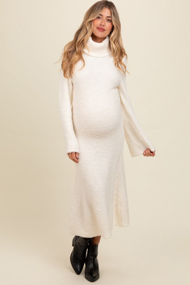 woman wearing a cream turtleneck maternity sweater dress with bell sleeves and a visible baby bump