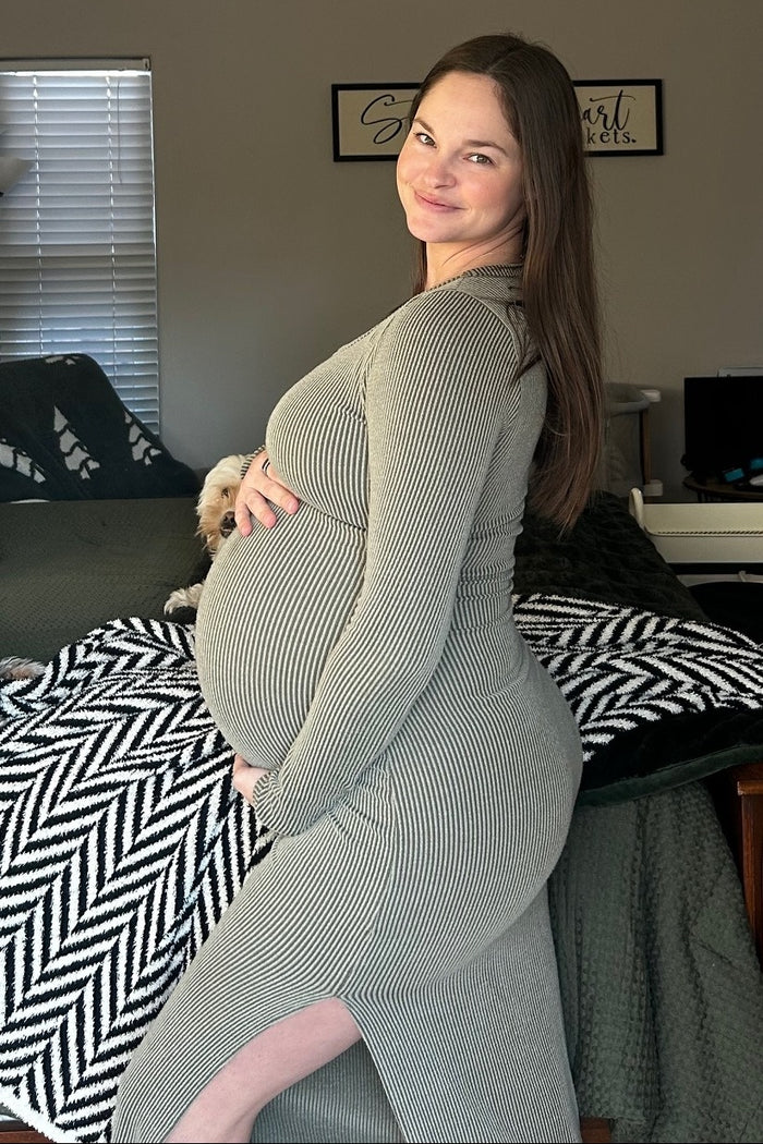 woman wearing a striped grey maternity dress, showing her pregnant belly with a side slit, posing with a smile