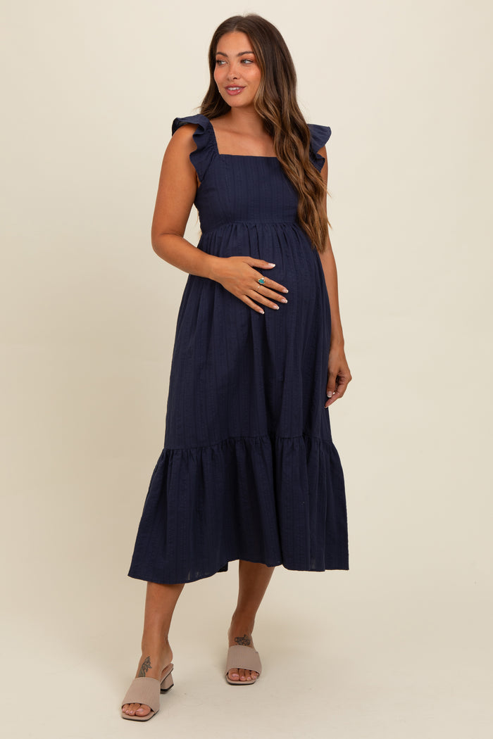 woman wearing a navy blue maternity dress with ruffle sleeves and a tiered skirt, showing her baby bump