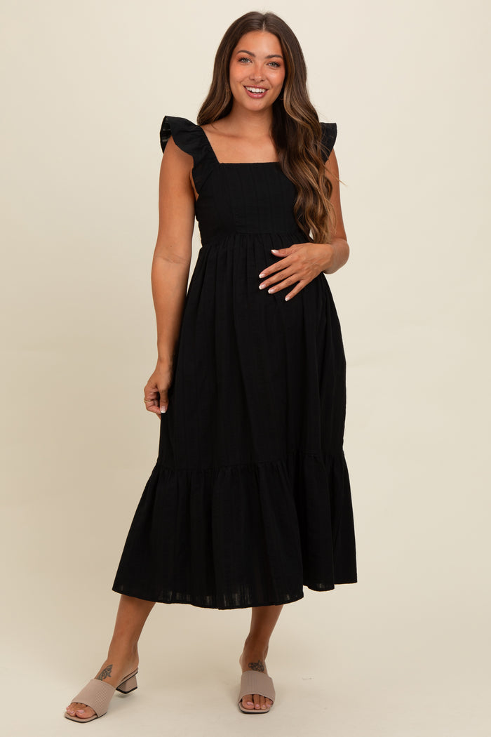 woman wearing a black maternity dress with ruffle straps and a tiered skirt, styled for comfort during pregnancy