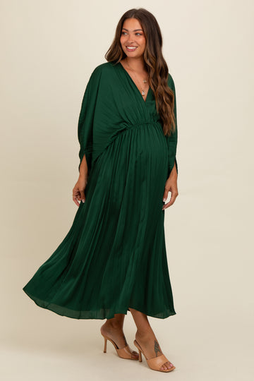woman wearing a flowing deep green maternity dress with a v-neckline and pleated details, showing her baby bump