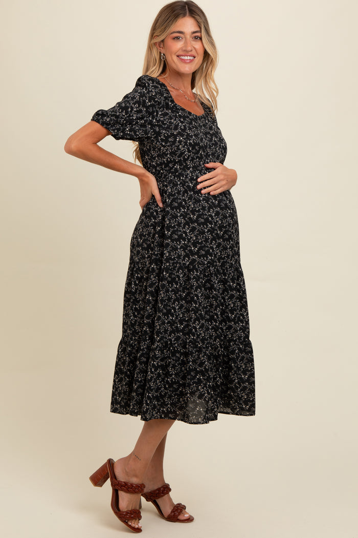 woman wearing a black floral maternity dress with short sleeves and a tiered skirt, showing her baby bump