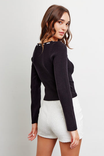 woman wearing a black fitted ribbed long sleeve top with back button detail and white sequined shorts