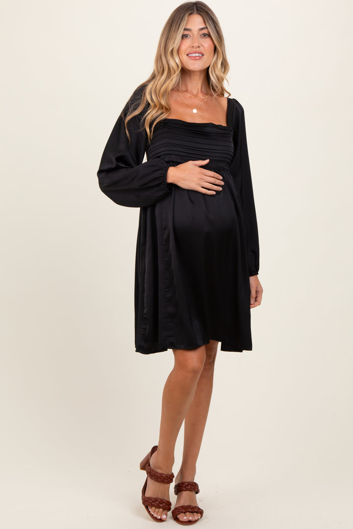 woman wearing a black off-the-shoulder maternity dress and holding her baby bump
