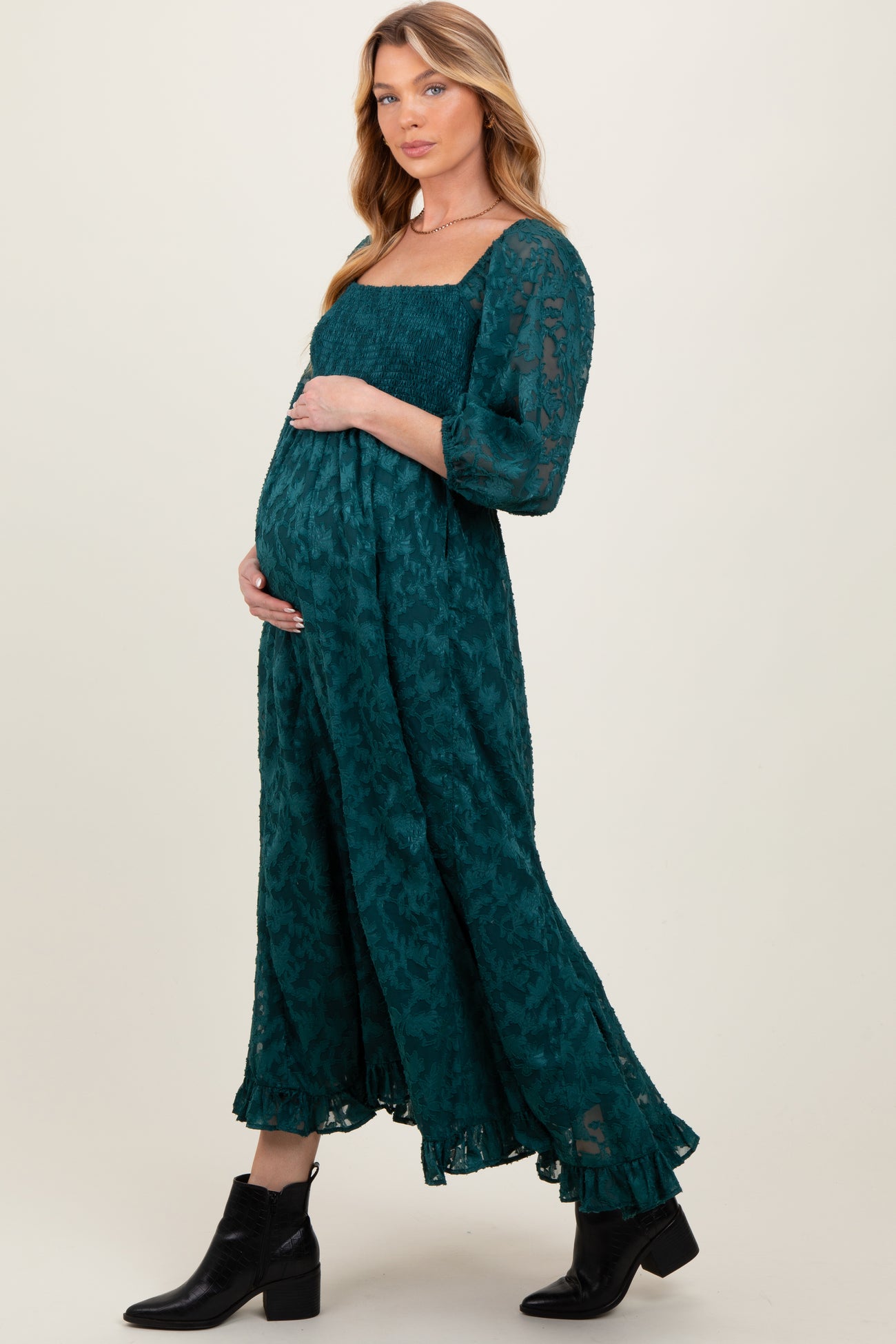 woman wearing a green floral print maternity dress with a square neckline and long sleeves, holding her baby bump