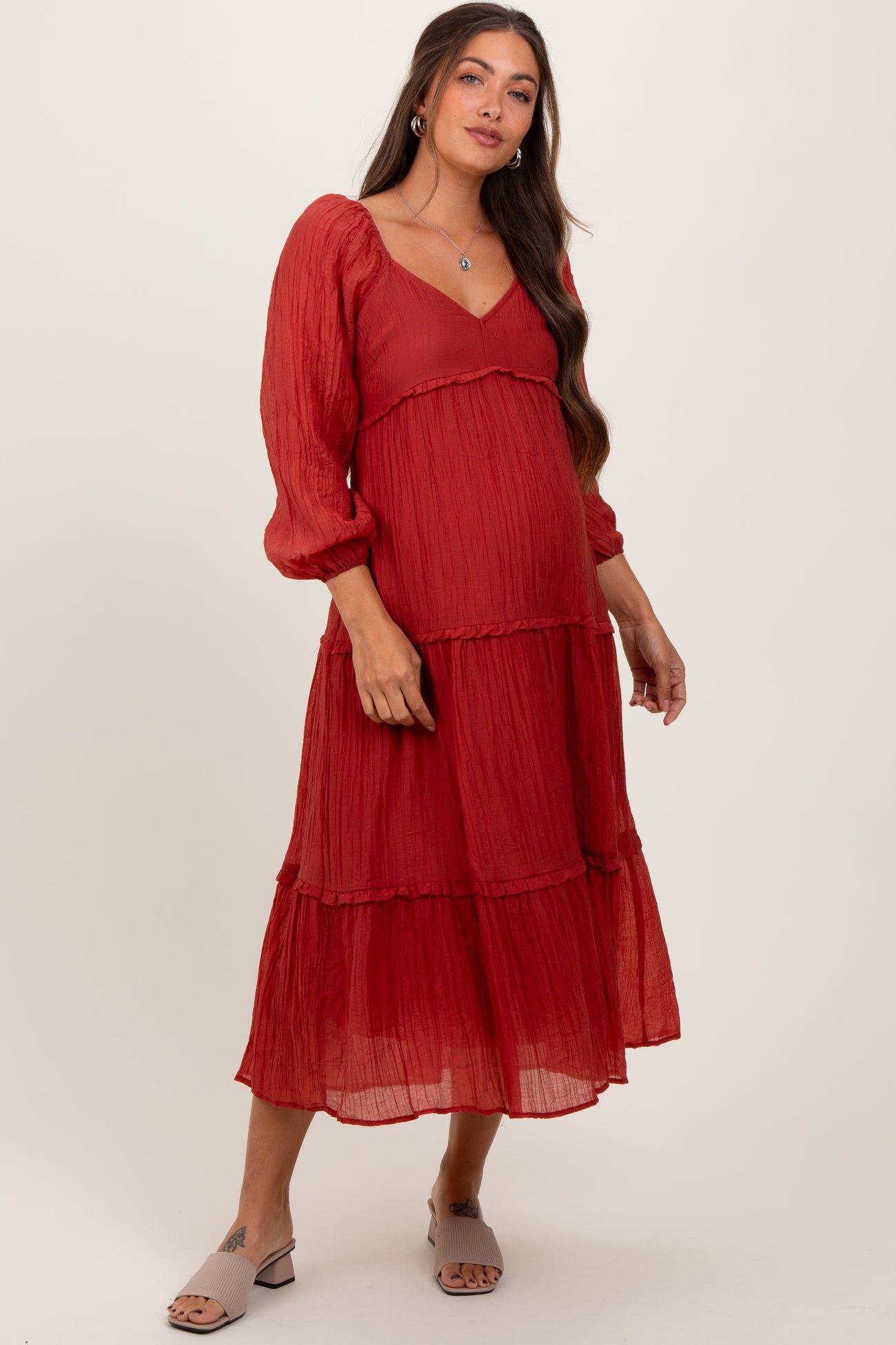 woman wearing a red tiered maternity dress with long puff sleeves and a sweetheart neckline, showing her baby bump