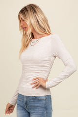 woman wearing a light beige long sleeve top with side ruche detail and paired with blue jeans