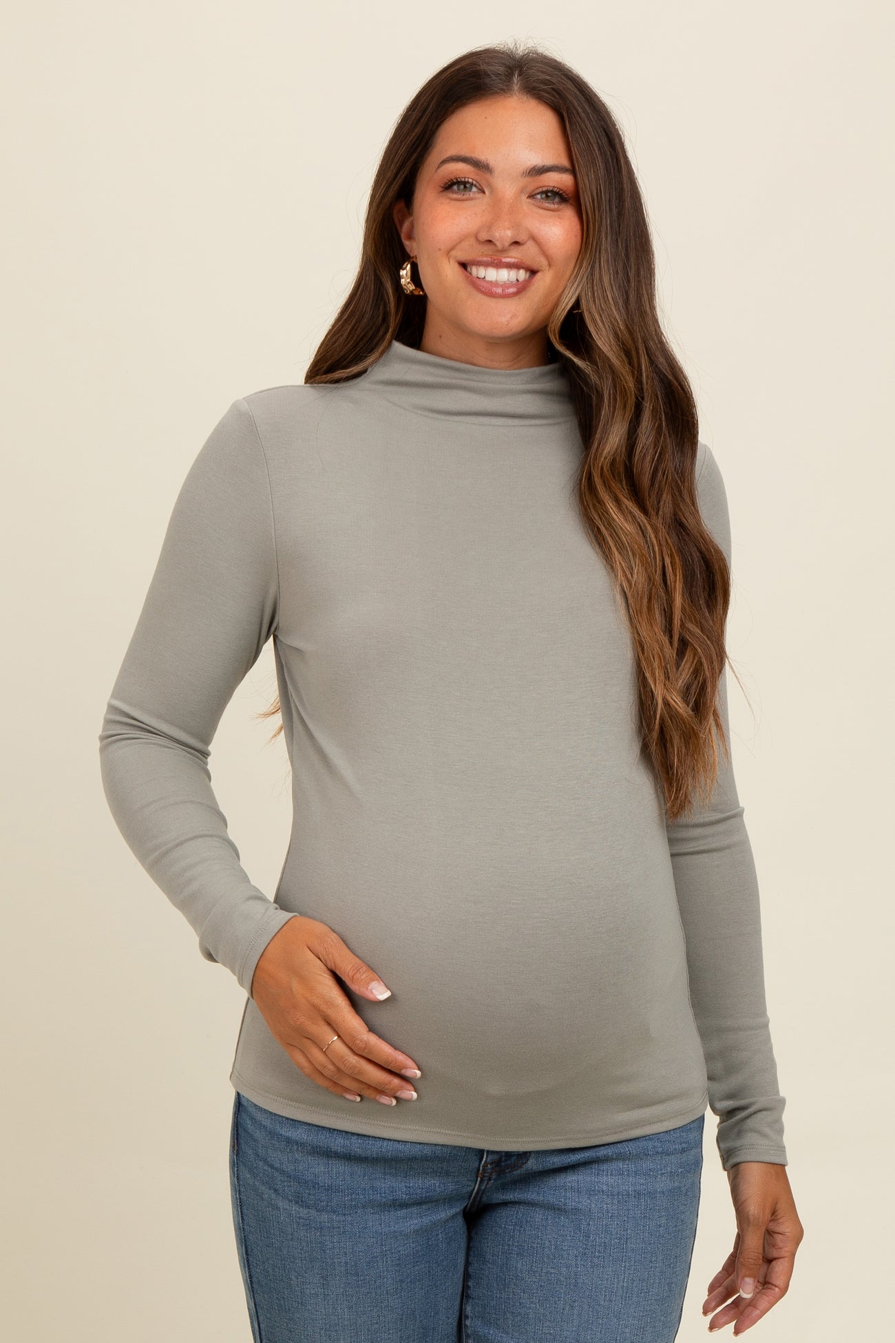 woman wearing a light grey long sleeve maternity top and showing her baby bump