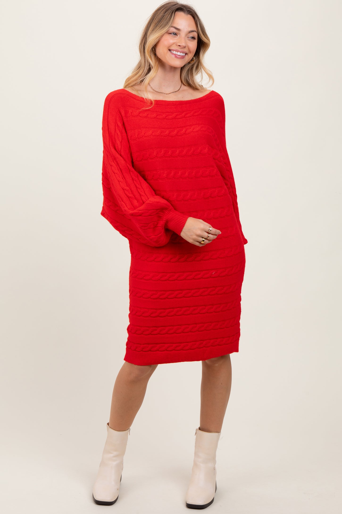 woman wearing a bright red cable knit sweater dress with long sleeves and a relaxed fit, paired with white ankle boots