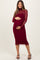 woman wearing a burgundy long sleeve maternity dress with sheer overlay and holding her baby bump