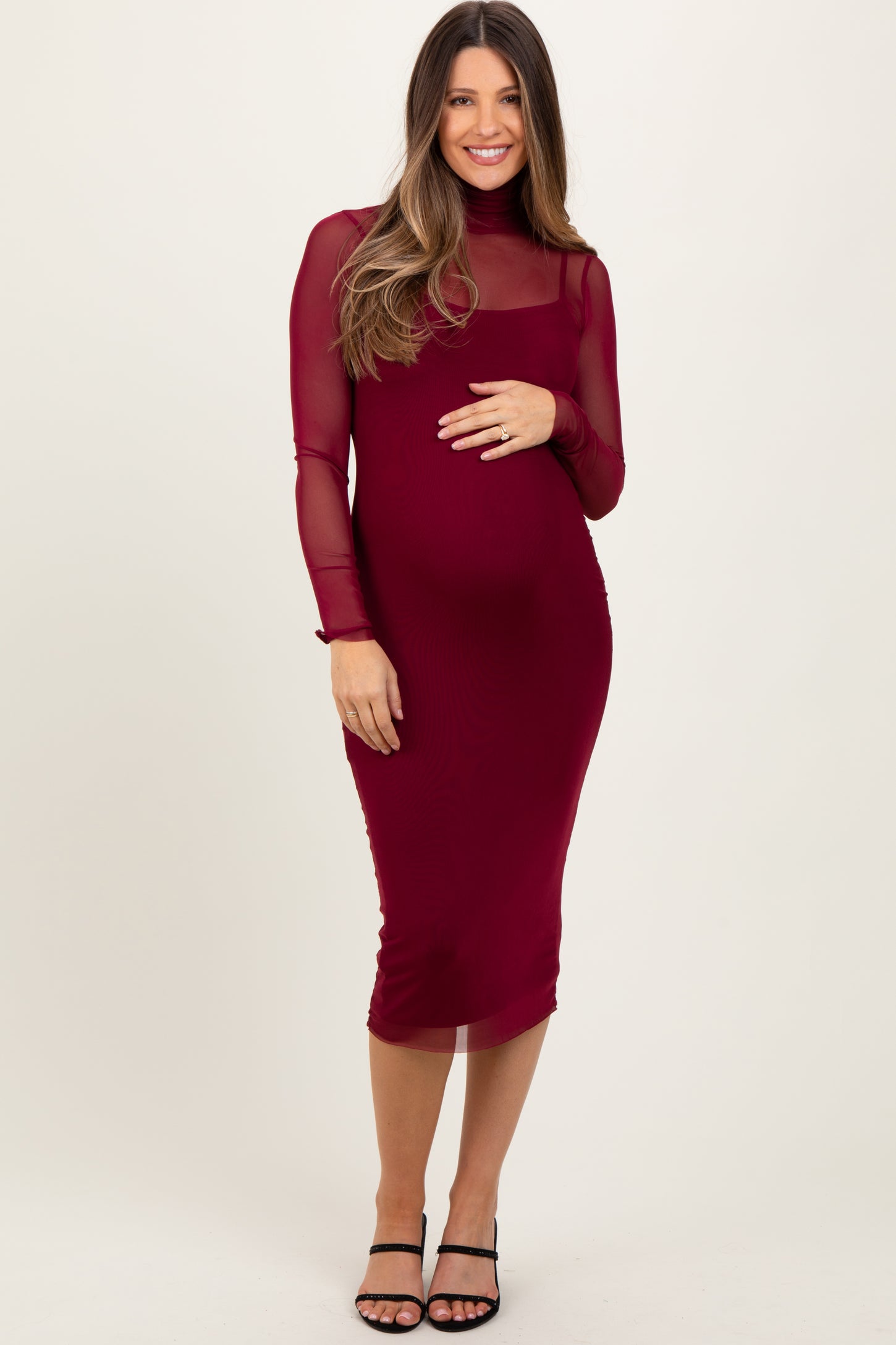 woman wearing a burgundy long sleeve maternity dress with a sheer overlay and a visible baby bump