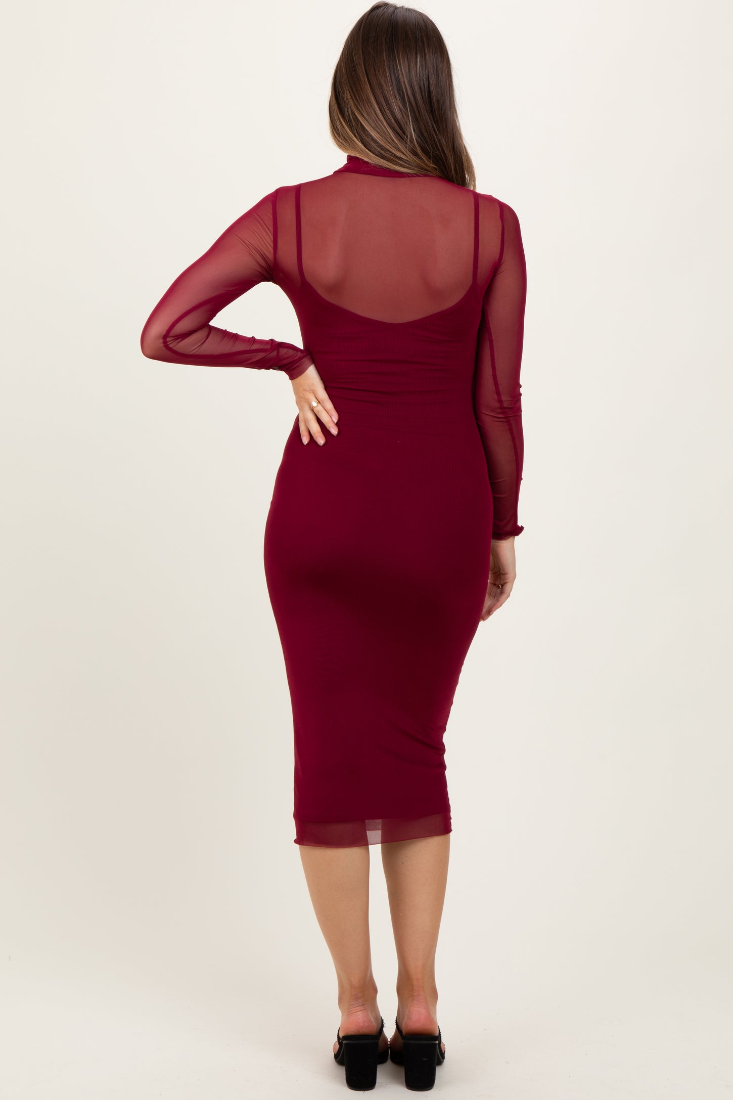 woman wearing a burgundy maternity dress with sheer long sleeves, showing her baby bump from the back