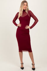 woman wearing a burgundy midi dress with sheer long sleeves and a high neck, posing confidently