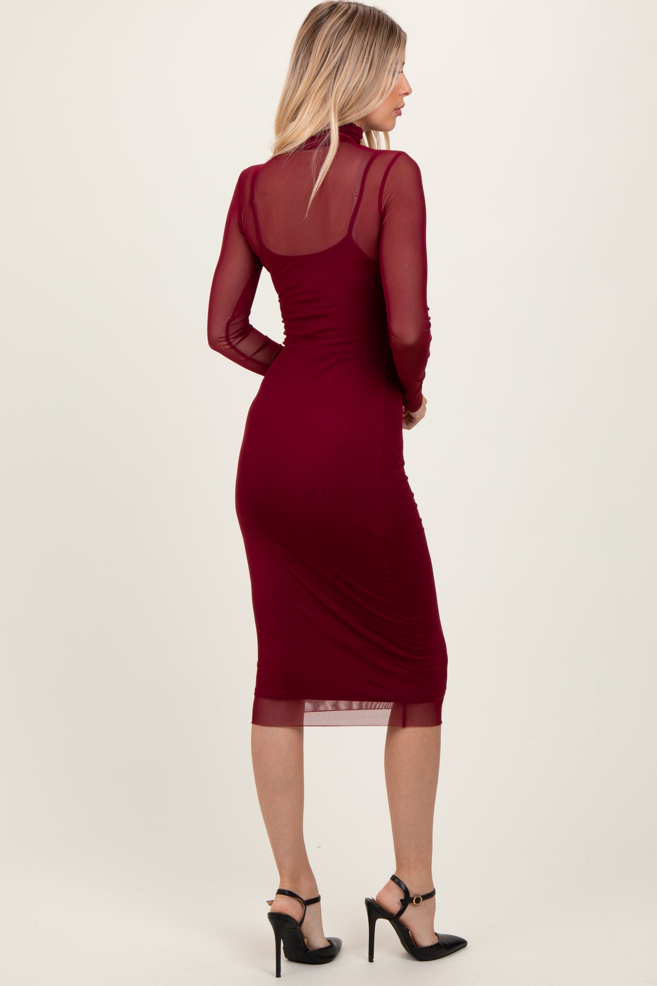 woman wearing a burgundy long sleeve midi dress with sheer details and a fitted silhouette, paired with black high heels