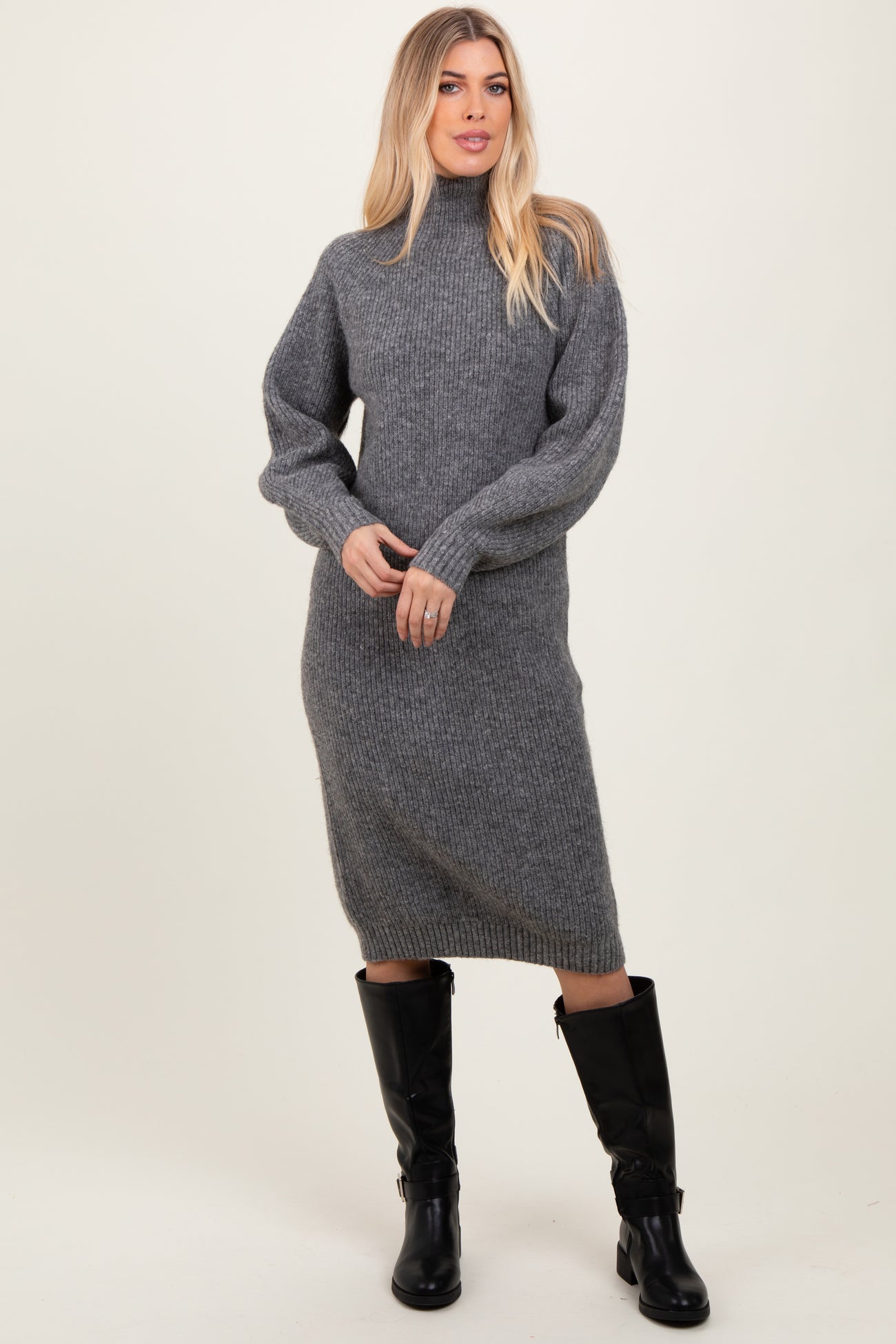 woman wearing a gray ribbed knit sweater dress with a high neckline and oversized sleeves, paired with black knee-high boots