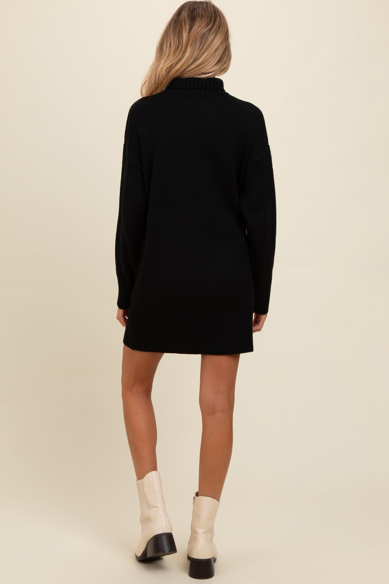 woman wearing a black oversized maternity sweater dress, featuring a high collar and long sleeves, with a view of the back