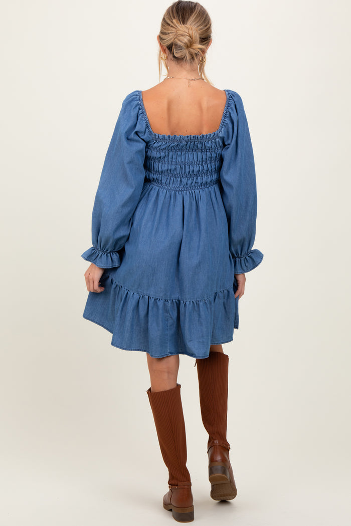 woman wearing a blue denim maternity dress with a smocked back and ruffled hem, paired with brown knee-high boots