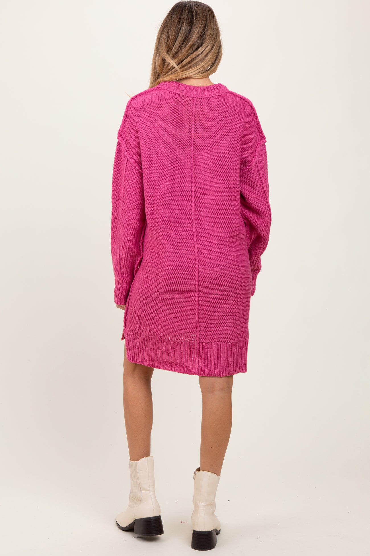 woman wearing a vibrant pink oversized maternity sweater dress, seen from the back, paired with white ankle boots
