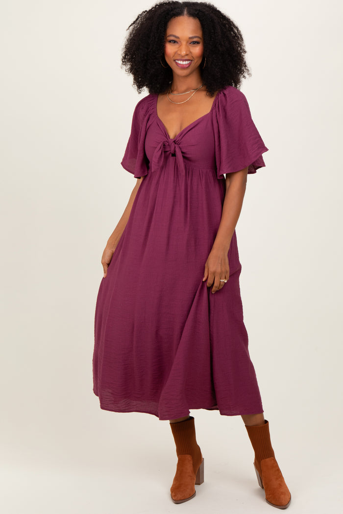 woman wearing a deep burgundy midi dress with a tie front and flutter sleeves, paired with brown ankle boots