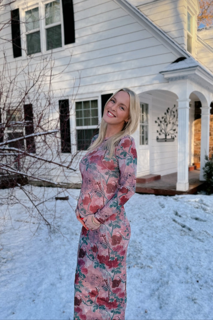 woman wearing a floral long sleeve maternity dress and showing her baby bump outside a house with snow on the ground