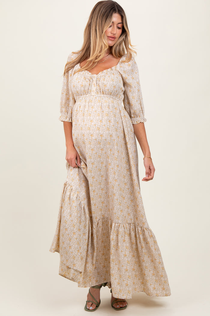 woman wearing a cream floral maternity maxi dress with puff sleeves and a tiered skirt, featuring a visible baby bump