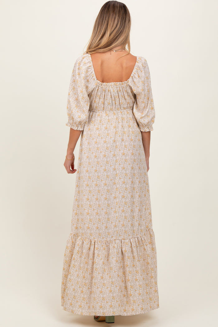 woman wearing a beige floral maternity maxi dress with puff sleeves and a ruffled hem, shown from the back