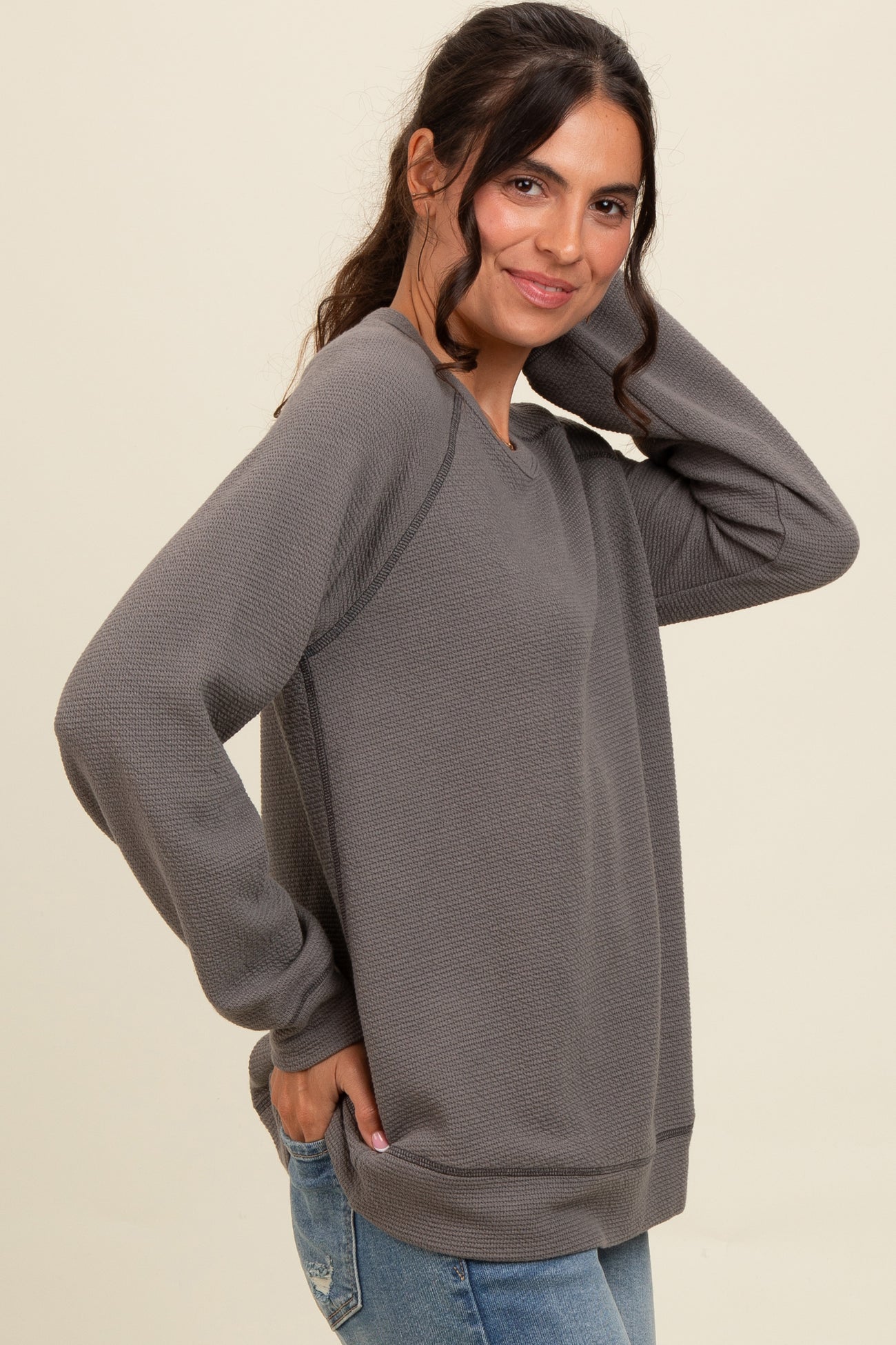 woman wearing a gray long sleeve sweatshirt with textured fabric and relaxed fit, posing with hand on her hair