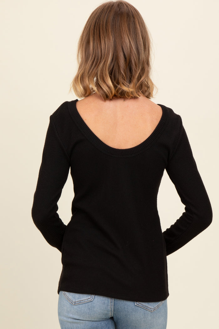woman wearing a black ribbed long sleeve top with a scoop back style, standing with her back to the camera