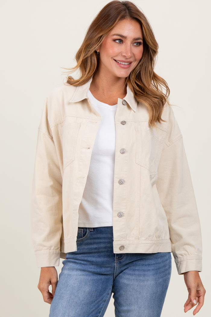 woman wearing a light beige oversized denim jacket with button closure and a white top, paired with blue jeans