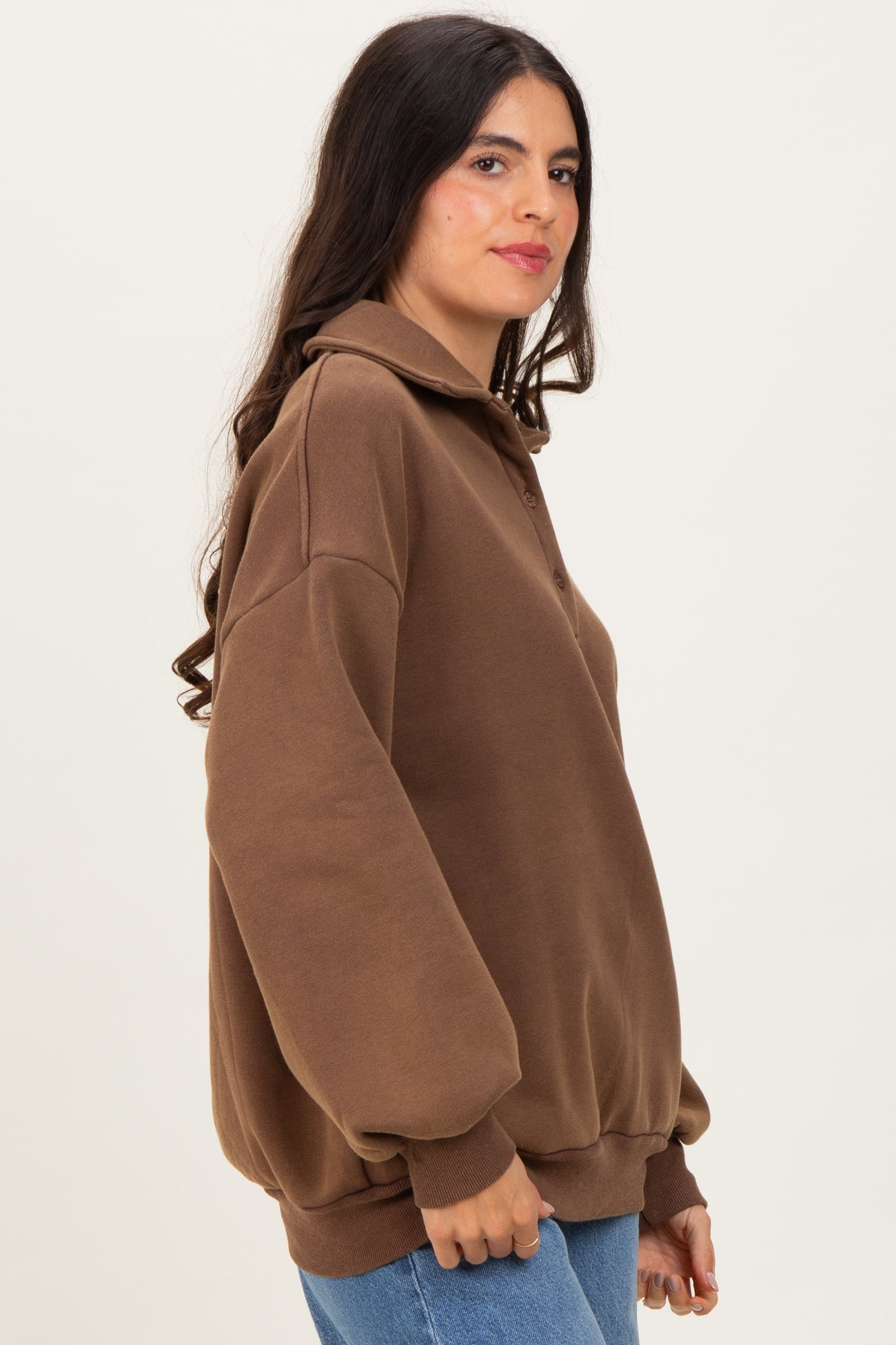 woman wearing a brown oversized pullover sweatshirt with a collar and button details, styled with denim jeans