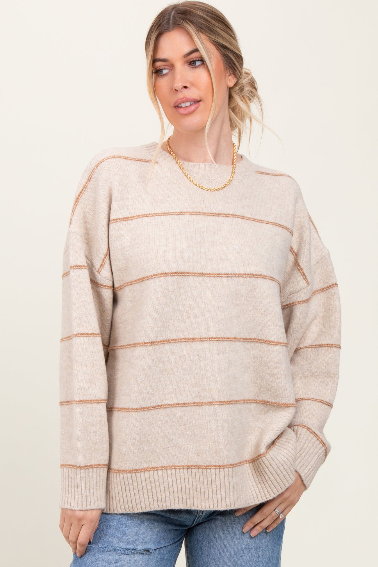 woman wearing a beige oversized sweater with rust-colored stripes and relaxed fit, styled with casual jeans