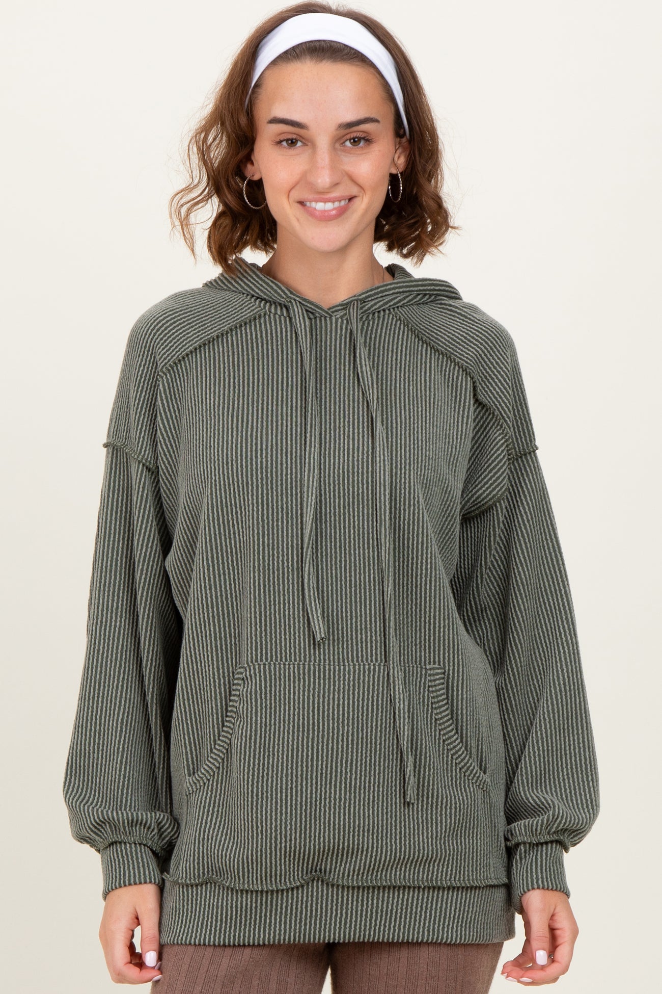 woman wearing an olive green striped oversized hoodie with a front pocket and drawstring hood