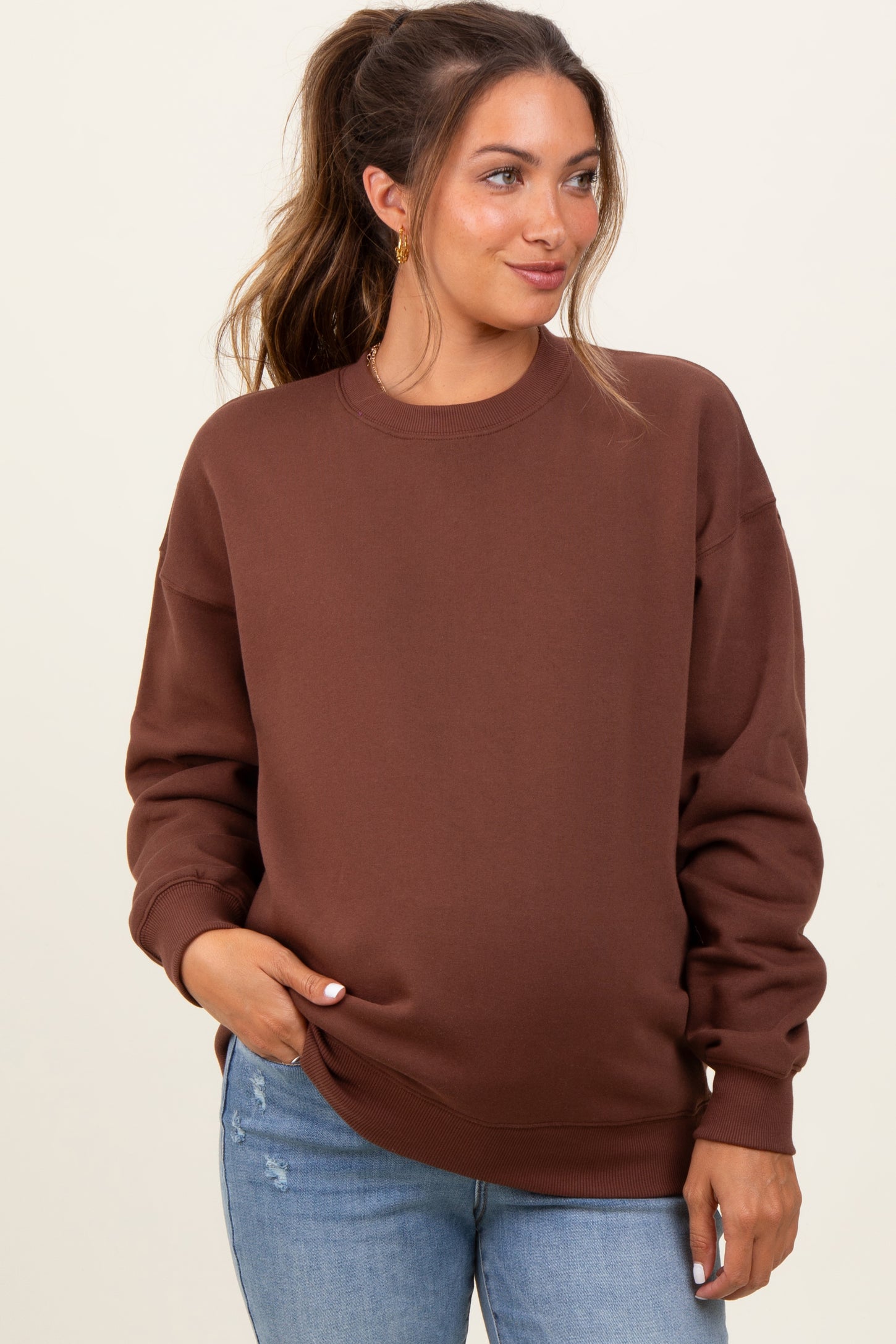 woman wearing a brown maternity sweatshirt with relaxed fit and long sleeves, paired with light blue jeans