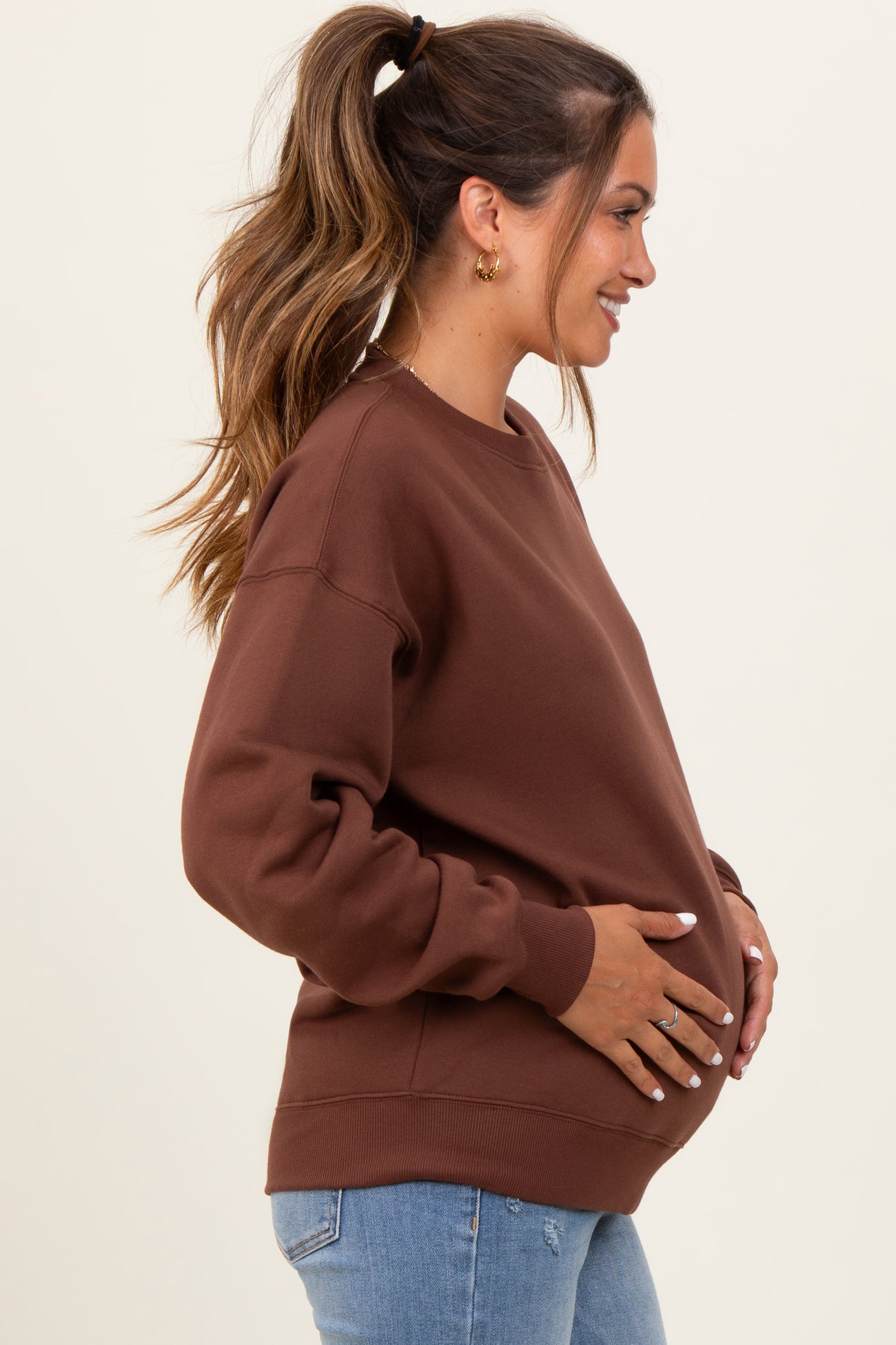woman wearing a brown maternity sweatshirt and holding her baby bump