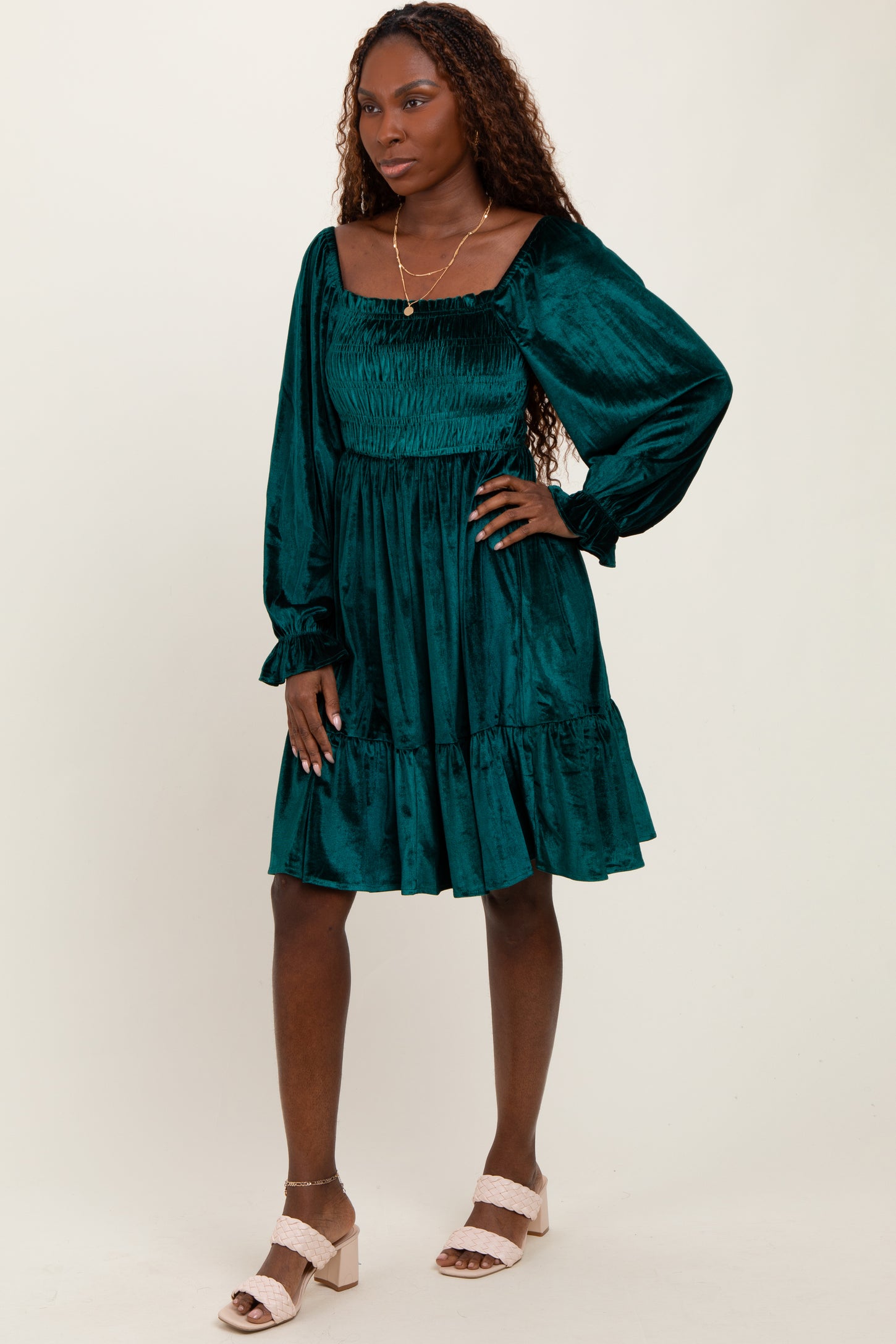 woman wearing a teal smocked mini dress with long sleeves and a ruffled hem, standing on a neutral background