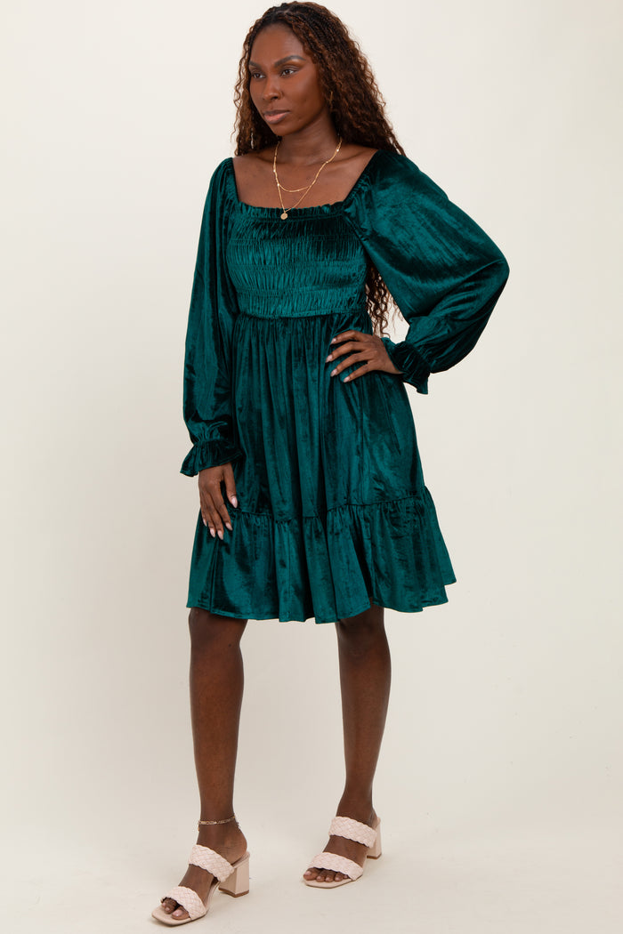 woman wearing a teal smocked mini dress with long sleeves and a ruffled hem, standing on a neutral background