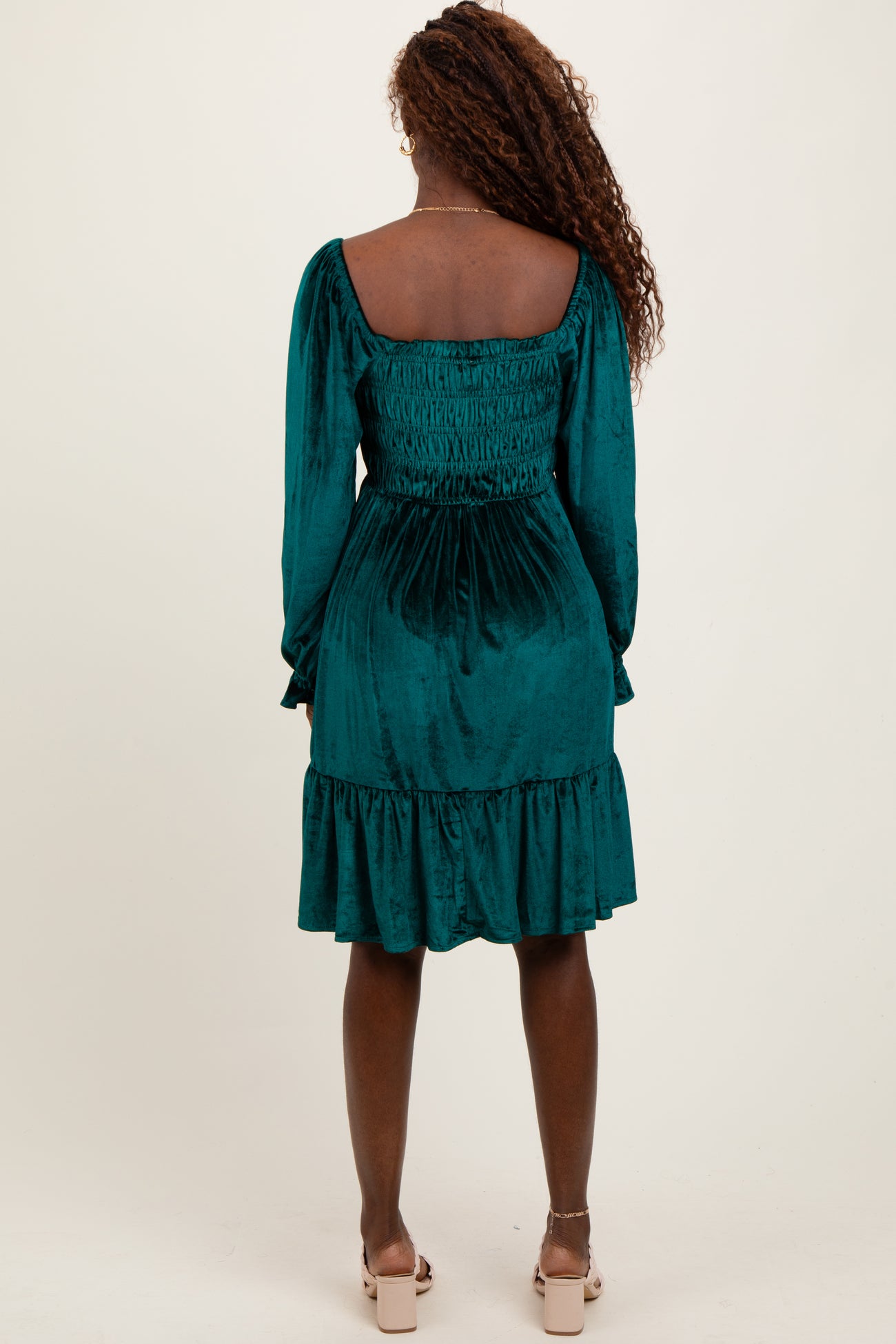 woman wearing a teal velvet smock dress with long sleeves and a ruffled hem, viewed from the back