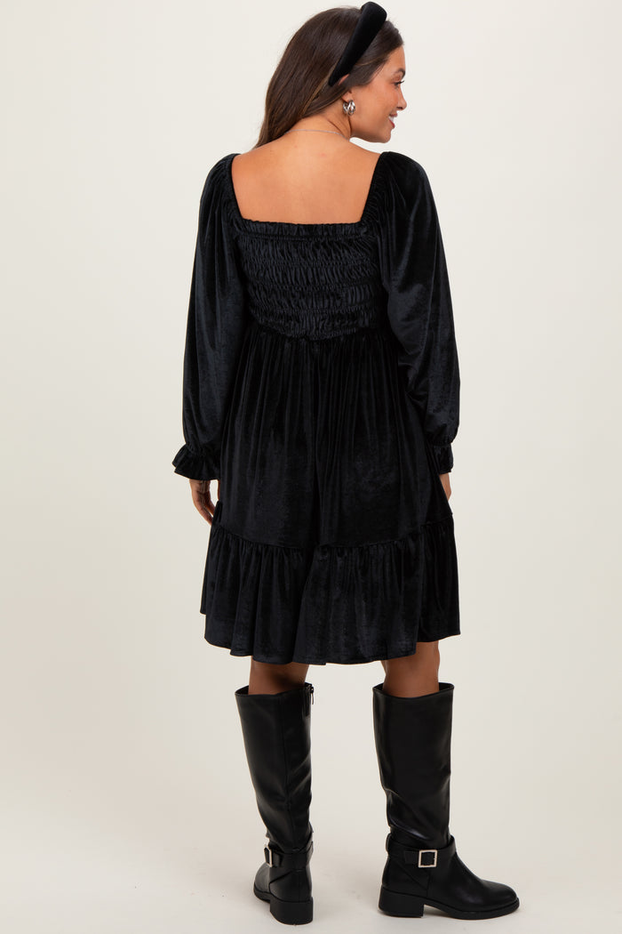 woman wearing a black velvet maternity dress with a smocked back and long sleeves, paired with knee-high black boots