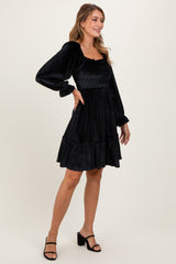 woman wearing a black smocked mini dress with long sleeves and a tiered skirt, posing sideways