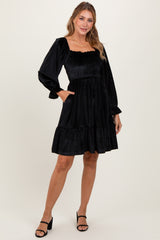 woman wearing a black smocked long sleeve dress with a tiered skirt and pockets, styled with strappy black heels