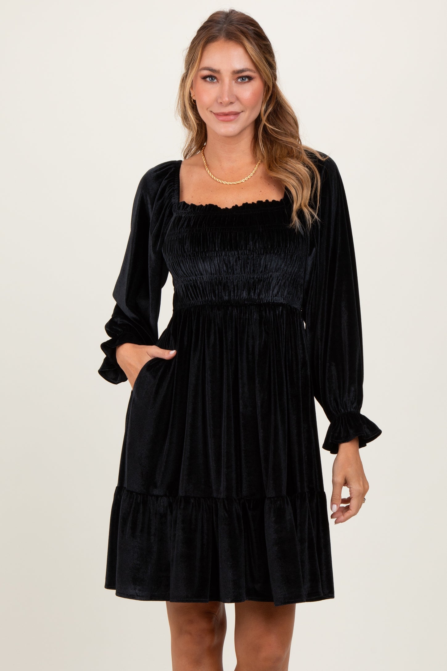 woman wearing a black velvet puff sleeve dress with a square neckline and tiered hem and pockets