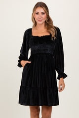 woman wearing a black velvet puff sleeve dress with a square neckline and tiered hem and pockets